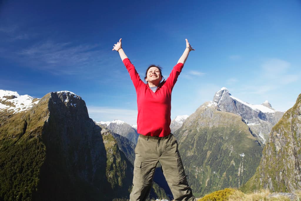 Transformation Man in a red top celebrating with arms raised in the mountains