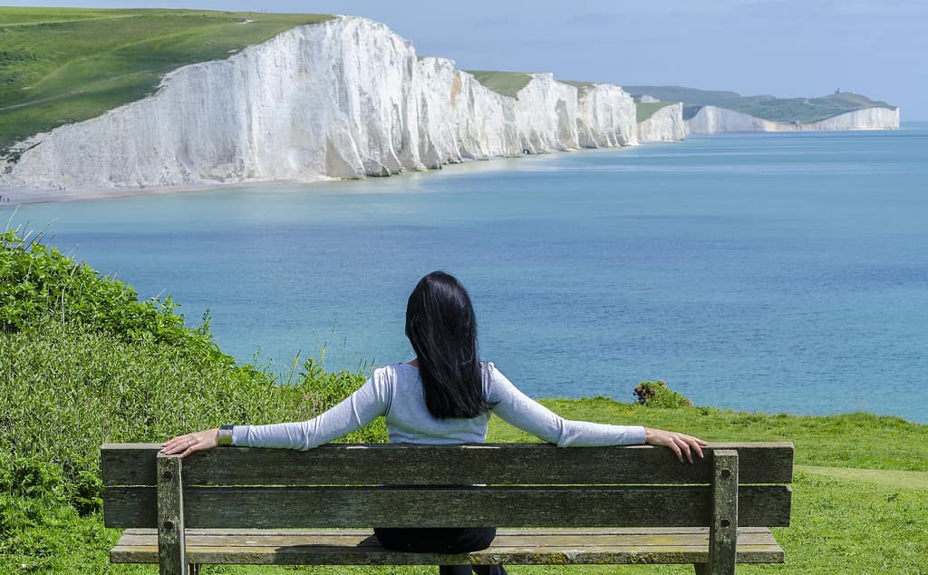 Face challenges with confidence Woman on a bench overlooking white chalk cliffs and the sea